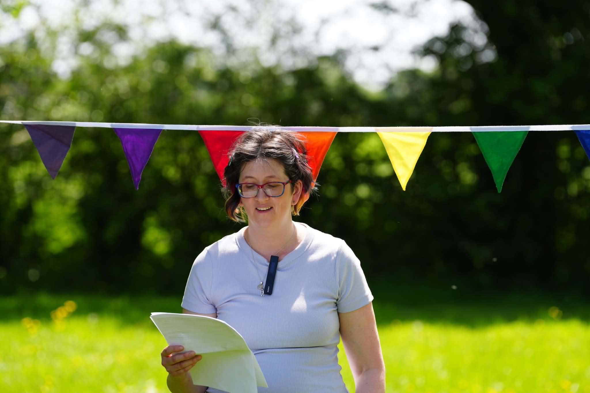 Celebrant leading an outdoor naming ceremony in a sunny field with rainbow bunting